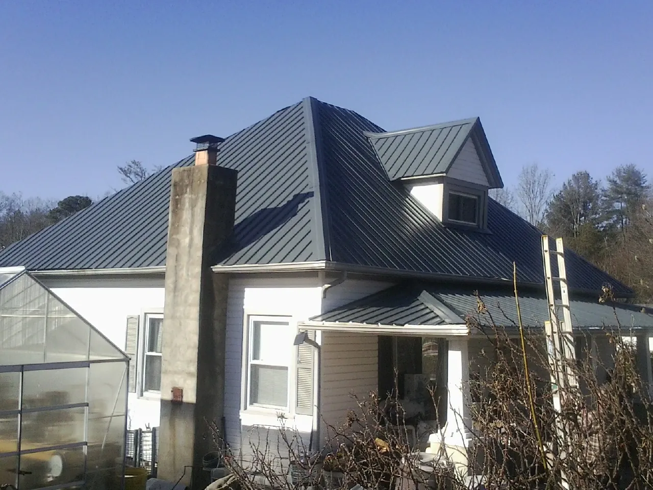 Dark blue standing seam metal roof on a white farmhouse with dormer — Slate & Tile Roof Repair by Roofing Brothers in East Alton