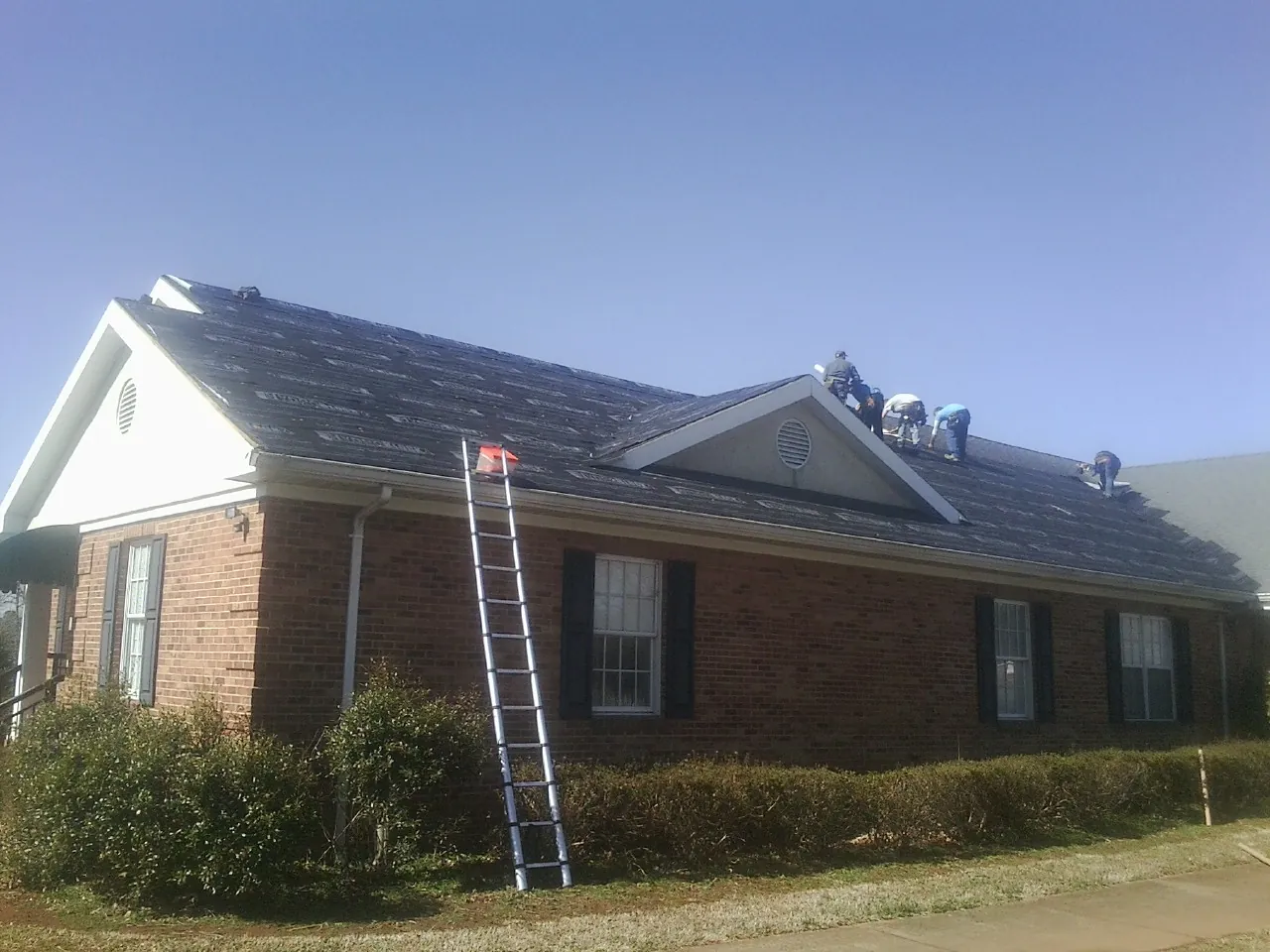 Crew tearing shingles off a brick ranch roof with a ladder set — Metal Roof Repair work by our crew in East Alton