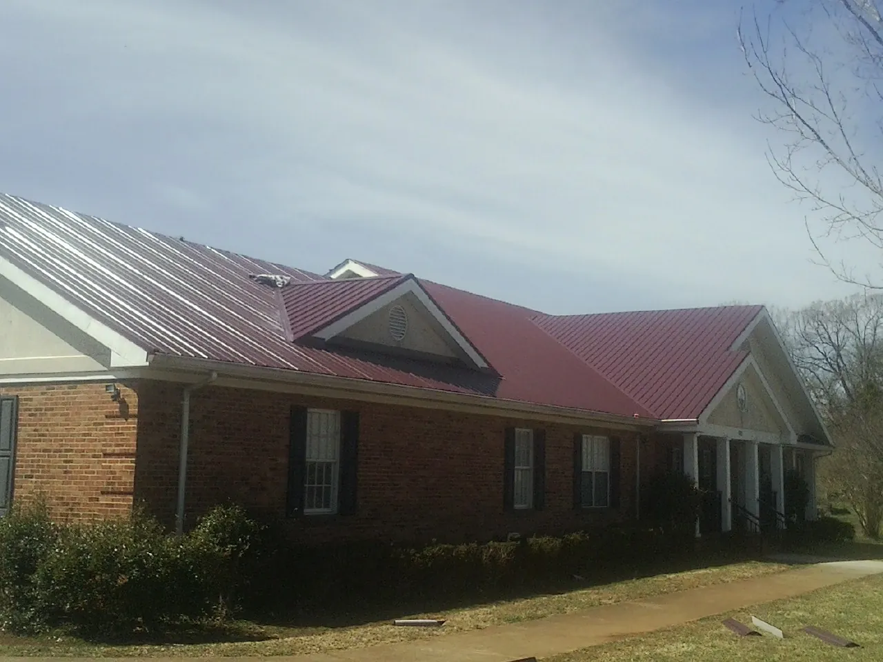 Red metal roof with gabled entries on a long brick building, from a Hail Damage Roof Repair job in East Alton