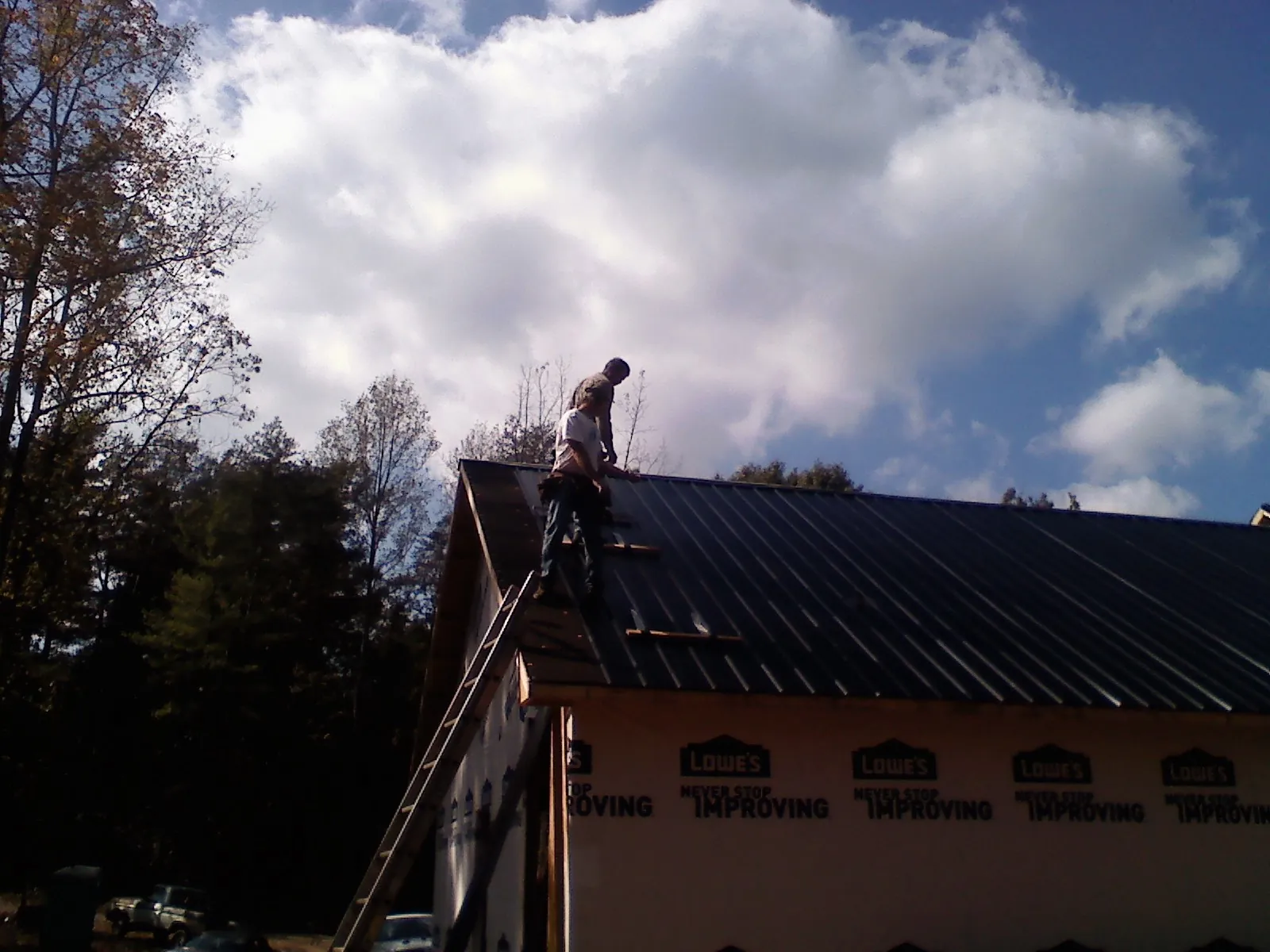 Roofer fastening dark metal panels high against a cloudy sky, from a Roof Inspection job in East Alton