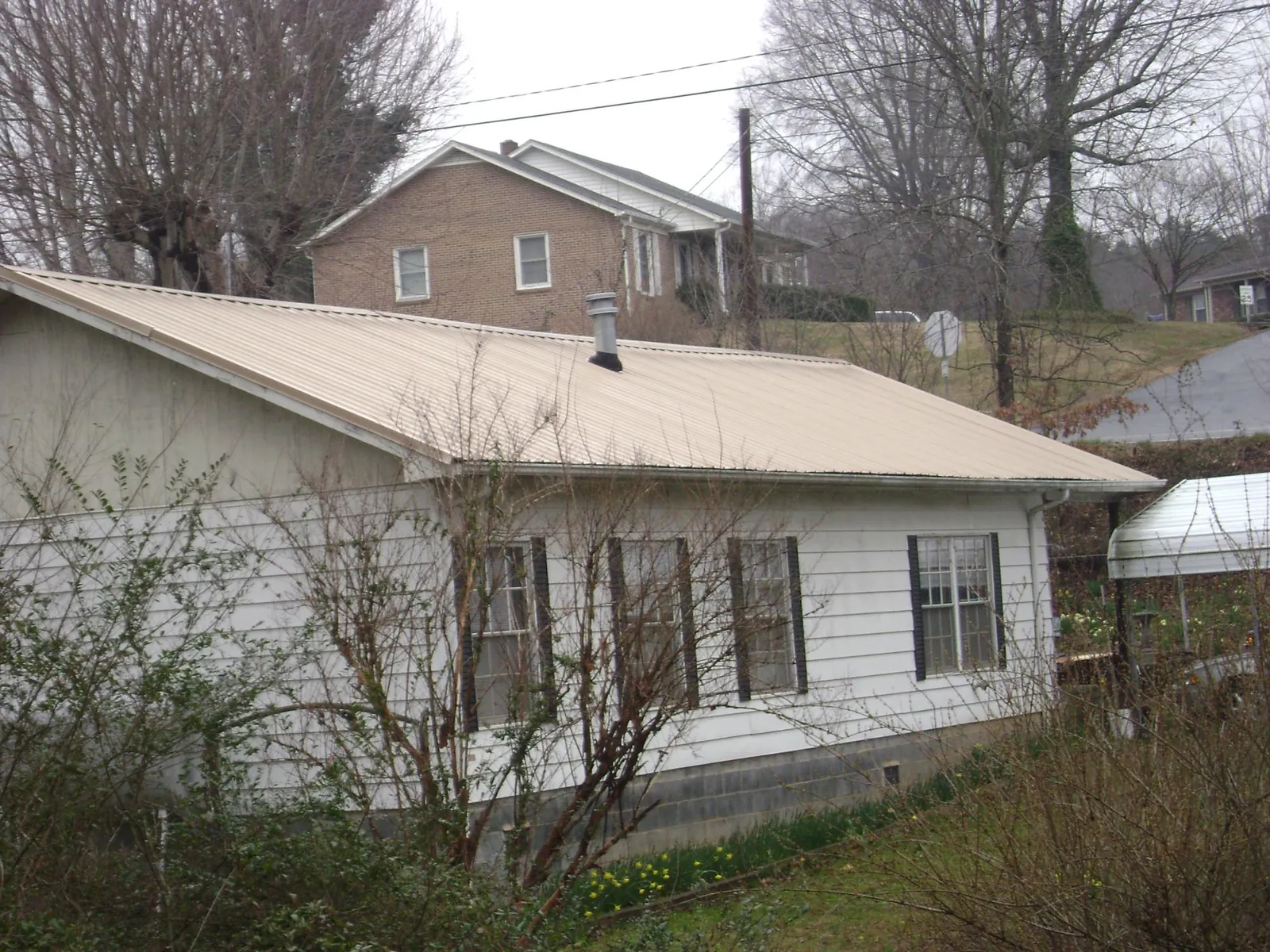 Tan metal roof on a white sided house set into a hillside — Commercial Roofing by Roofing Brothers in East Alton